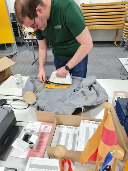 Jeffrey Paulus, stellvertretender Vorsitzender der DSJ, bügelt die Länderflagge von Sachsen-Anhalt und nutzt als Unterlage einen DSJ Hoodie.